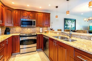 Una cucina moderna con mobili in legno, piani di lavoro in granito, elettrodomestici in acciaio inossidabile e illuminazione a sospensione.