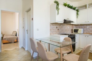 A compact kitchen with a glass dining table, white cabinets, and a microwave. - Dione Apartment with Terrace near Kalathas beach (Chania)