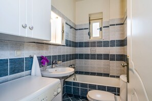 A bathroom with a white sink, a bathtub, and a toilet. There is a mirror above the sink and a towel hanging on the wall. - Dione Apartment with Terrace near Kalathas beach (Chania)