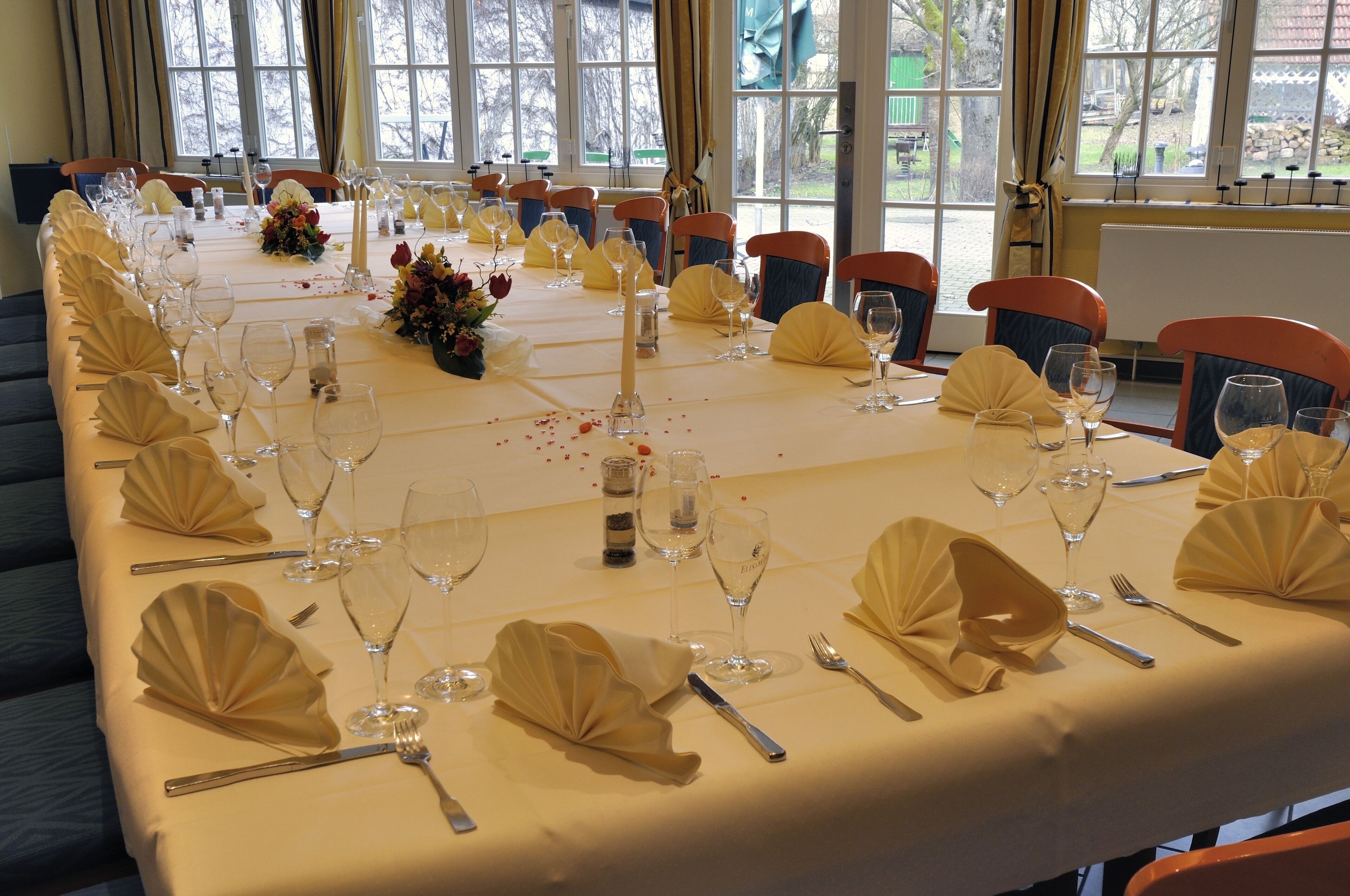 A long dining table set for a formal event with chairs, glassware, and a centerpiece.