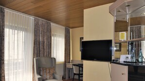 Hotellihuone, jossa on puinen katto, televisio, työpöytä, tuoli ja minibaari.