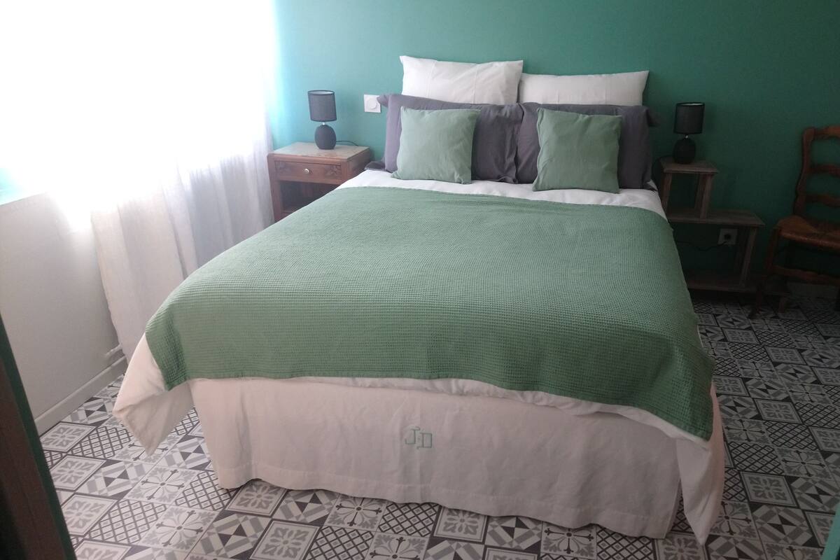 Un dormitorio con una cama, dos mesitas de noche, una silla y un suelo estampado.