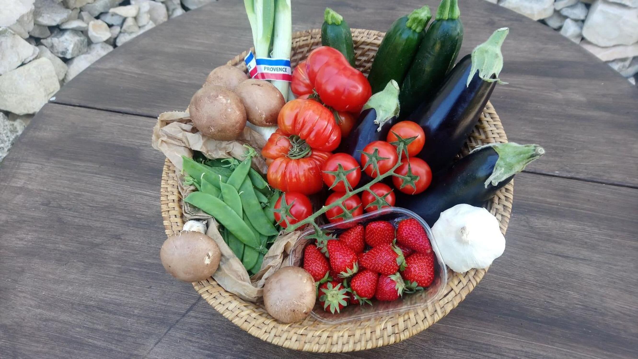 Un panier rempli de légumes frais, notamment des tomates, des aubergines et des champignons, posé sur une table en bois.