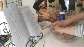 Une personne prépare un plat en utilisant un saladier rempli d’ingrédients et une fiche de recette posée sur le plan de travail.
