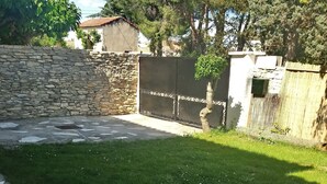 Un mur de pierres, une terrasse dallée et une pelouse, le tout délimité par une clôture et agrémenté d’arbres en arrière-plan.