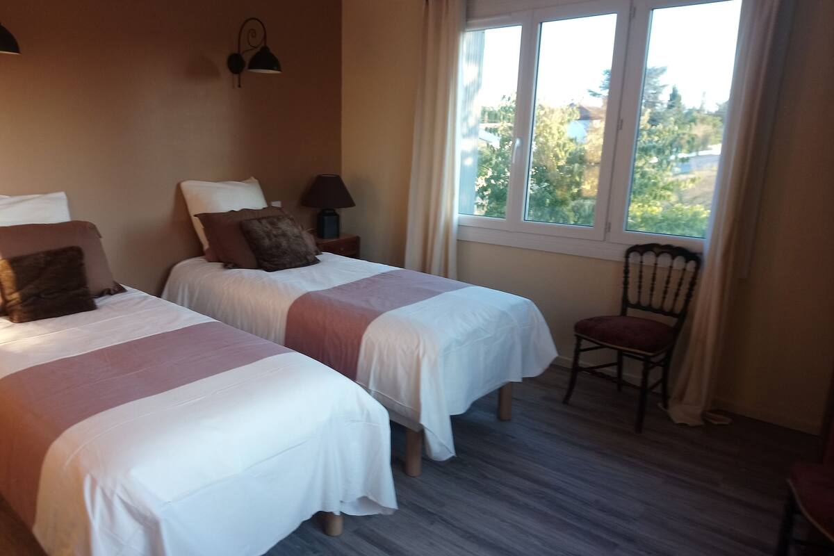 Un dormitorio con dos camas, una silla y una ventana con vistas a árboles.