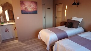 Une chambre d’hôtel avec deux lits, une salle de bain avec un rideau de douche, un tableau au mur et un miroir au-dessus du lavabo.
