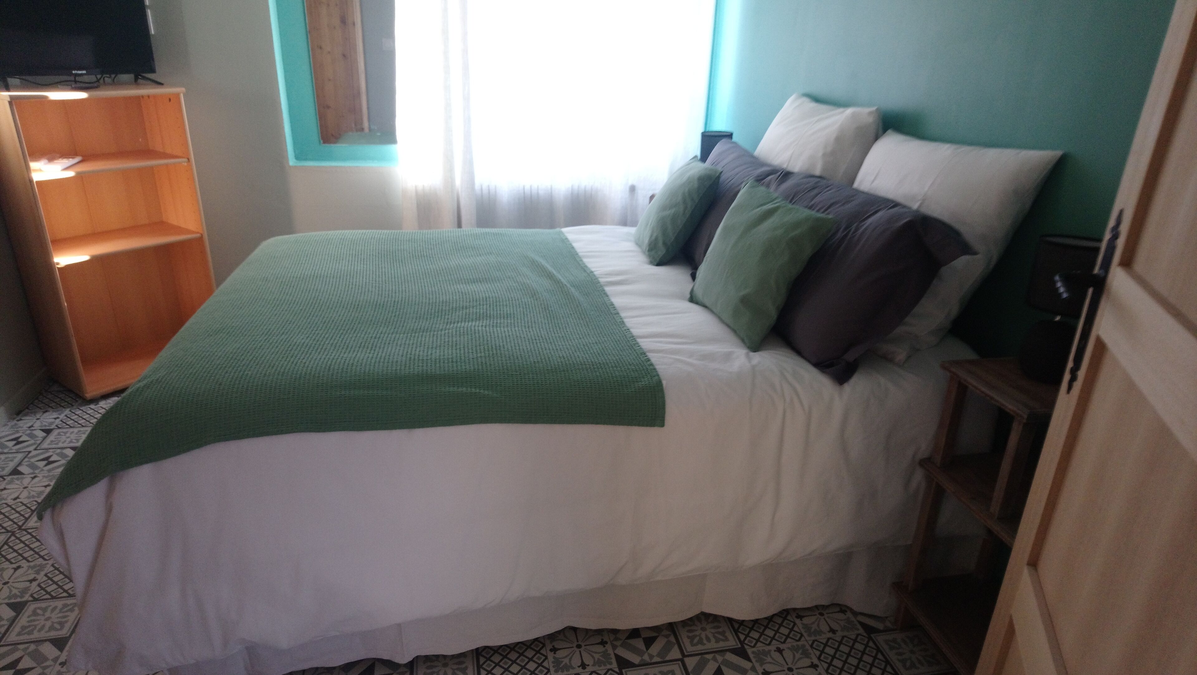 A bedroom with a bed, a green throw blanket, and a wooden shelf unit.