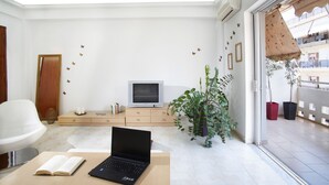 A modern living room with a laptop on a table, a TV on a wooden cabinet, and a large window with a view of buildings. - Dream City Apartment near Beach & Venetian Port (Chania)
