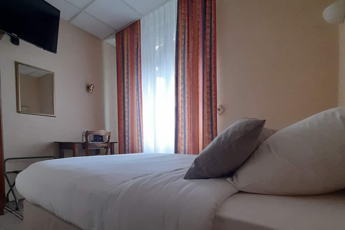 A hotel room with a large bed, a desk, a chair, a television mounted on the wall, and a window with curtains.