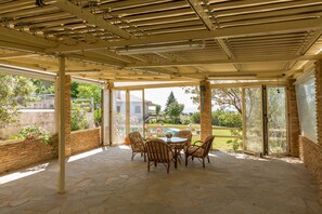 A covered patio with stone flooring, wicker chairs, and a table. - Dream Holidays in a Luxurious Garden Pool Villa (Pallini)