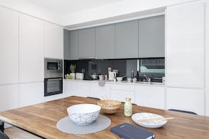 Una cocina moderna con armarios blancos, una mesa de comedor de madera y un horno empotrado.