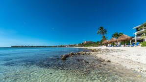 Una spiaggia con acque poco profonde e cristalline, una battigia sabbiosa e una fila di ombrelloni di paglia.