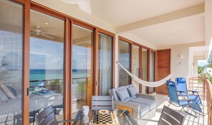 A spacious balcony with a glass table, a hammock, and outdoor seating. - Comfortable, modern condo with beautiful ocean views, swimming pool, AC! (Akumal)