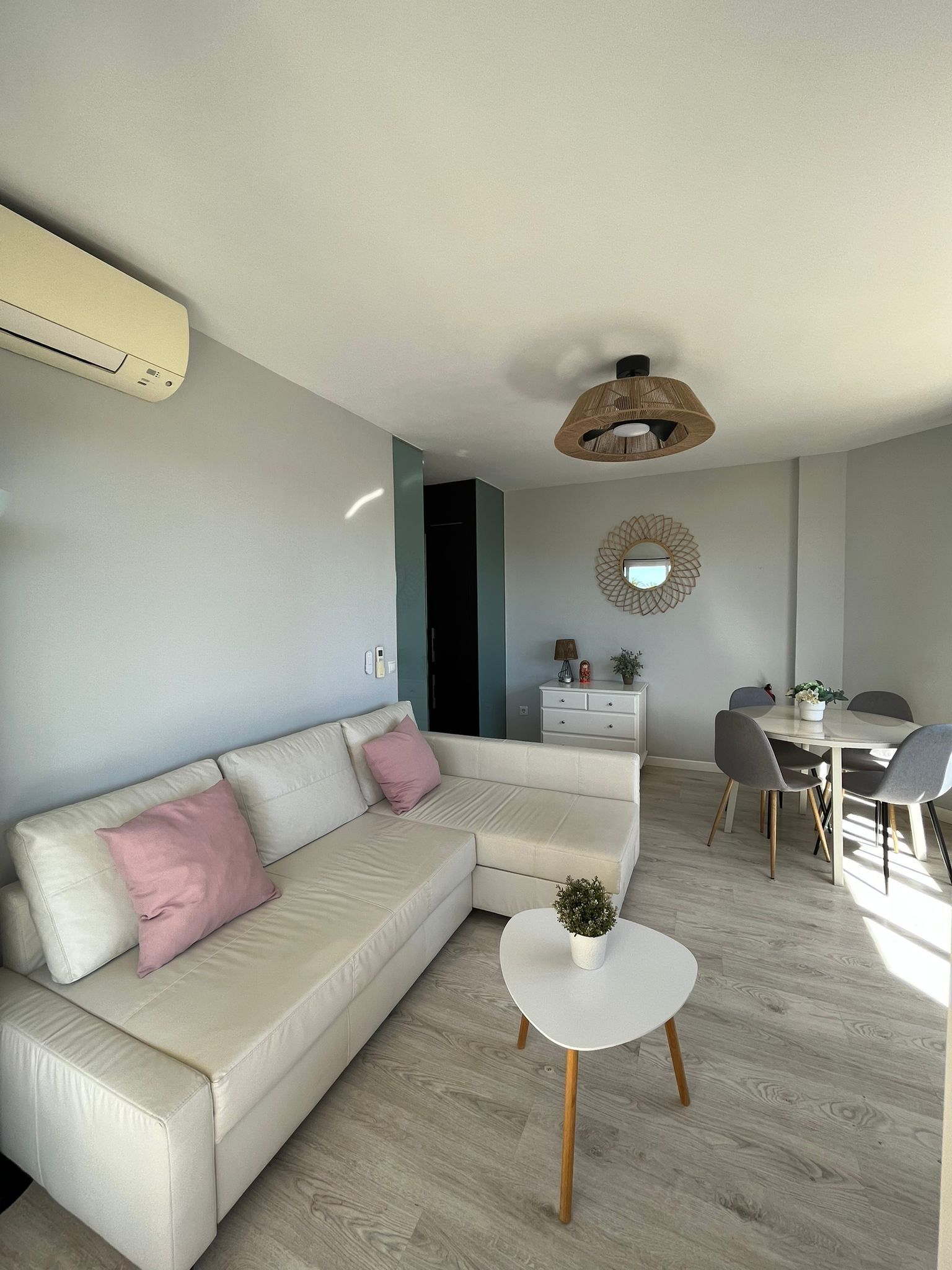 Ein modernes Wohnzimmer mit einem beigefarbenen Ecksofa, einem kleinen runden Tisch und einem Essbereich mit rundem Tisch und Stühlen.