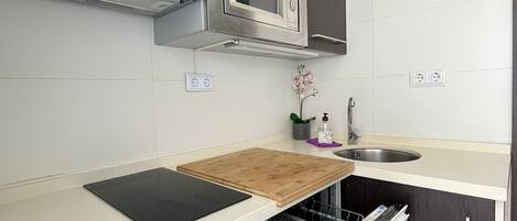 A modern kitchen with dark cabinetry, a stainless steel microwave, a wooden cutting board, and a dishwasher.