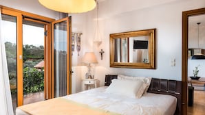 Ein Schlafzimmer mit Bett, Nachttisch, Lampe, Spiegel und Blick ins Freie.
