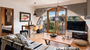 Ein modernes Wohnzimmer mit einer Couch, einem Esstisch, Stühlen, einem Fernseher und einem großen Fenster mit Blick auf Grünflächen.