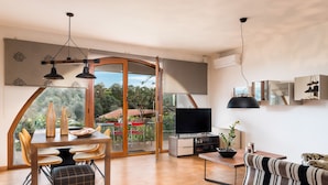 Ein modernes Wohnzimmer mit Essbereich, großen Fenstern und einem Fernseher.