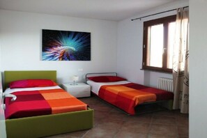 Una habitación con dos camas, una mesita de noche, una ventana con cortinas y un cuadro colgado en la pared.