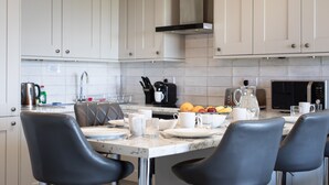 A modern kitchen with white cabinets, a marble countertop, and black leather chairs. - Fantastic Location with Stunning Estuary Views (Deganwy)