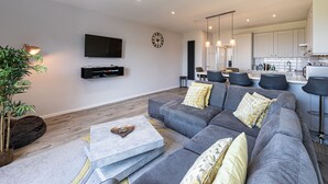 A modern living room with a grey sofa, a coffee table, and a flat-screen TV mounted on the wall. - Fantastic Location with Stunning Estuary Views (Deganwy)