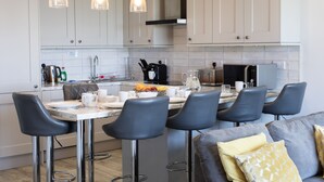 A modern kitchen with white cabinets, a marble countertop, and bar stools. - Fantastic Location with Stunning Estuary Views (Deganwy)