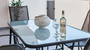 Une table en verre sur laquelle se trouvent une bouteille de vin et un verre, un bol décoratif et une chaise.
