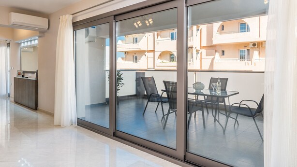 Une chambre d’hôtel moderne dotée d’un balcon, d’un coin repas avec des chaises et une table, ainsi que d’un comptoir de réception.