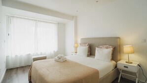 A hotel room with a large bed, two bedside tables with lamps, a bench, and a window with sheer curtains. - Savory Blue Apartment, Wifi, Garage, Lift!New! (Lisboa)