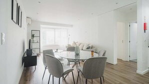 A modern living room with a round glass table, grey chairs, a sofa, and a bookshelf. - Savory Blue Apartment, Wifi, Garage, Lift!New! (Lisboa)
