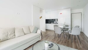 A modern living room with a sofa, a dining table with chairs, and a kitchen area in the background. - Savory Blue Apartment, Wifi, Garage, Lift!New! (Lisboa)