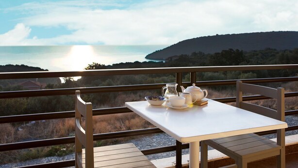Un balcon avec une table dressée pour le thé, offrant une vue panoramique sur la mer et les collines.