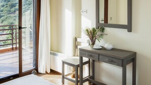Une chambre d’hôtel avec un balcon, une petite table ornée d’un vase et d’une théière, une chaise et un grand miroir au mur.