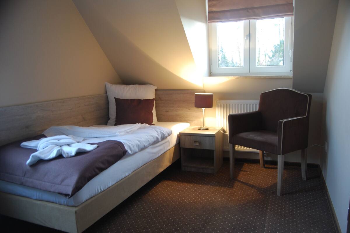 Un dormitorio con una cama, una silla, una mesita de noche, una lámpara y una ventana.
