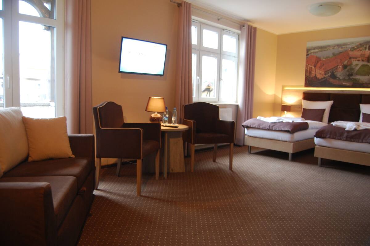 Una habitación de hotel con una cama, un sofá, un escritorio con lámpara y una televisión.