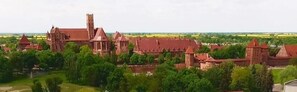 Un grand bâtiment historique doté de nombreuses tours, dont une tour centrale imposante, et entouré d’une végétation luxuriante.