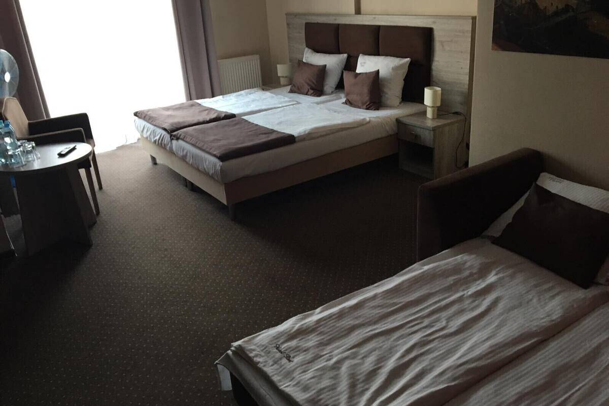 Habitación de hotel con una cama grande, otra más pequeña, un escritorio con silla, una lámpara y un cuadro en la pared.