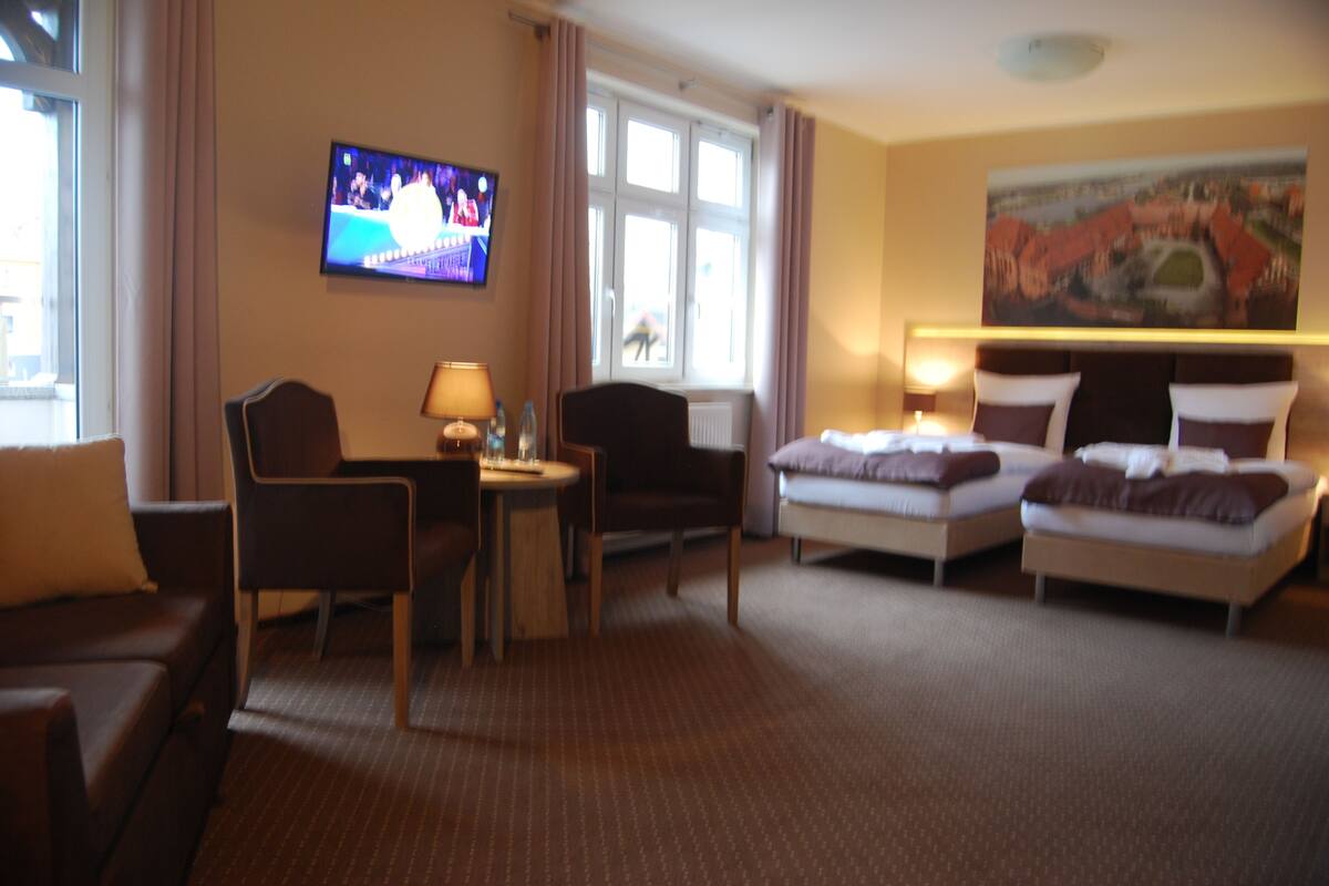 Una habitación de hotel con televisión, un cuadro, una cama, un escritorio y una silla.