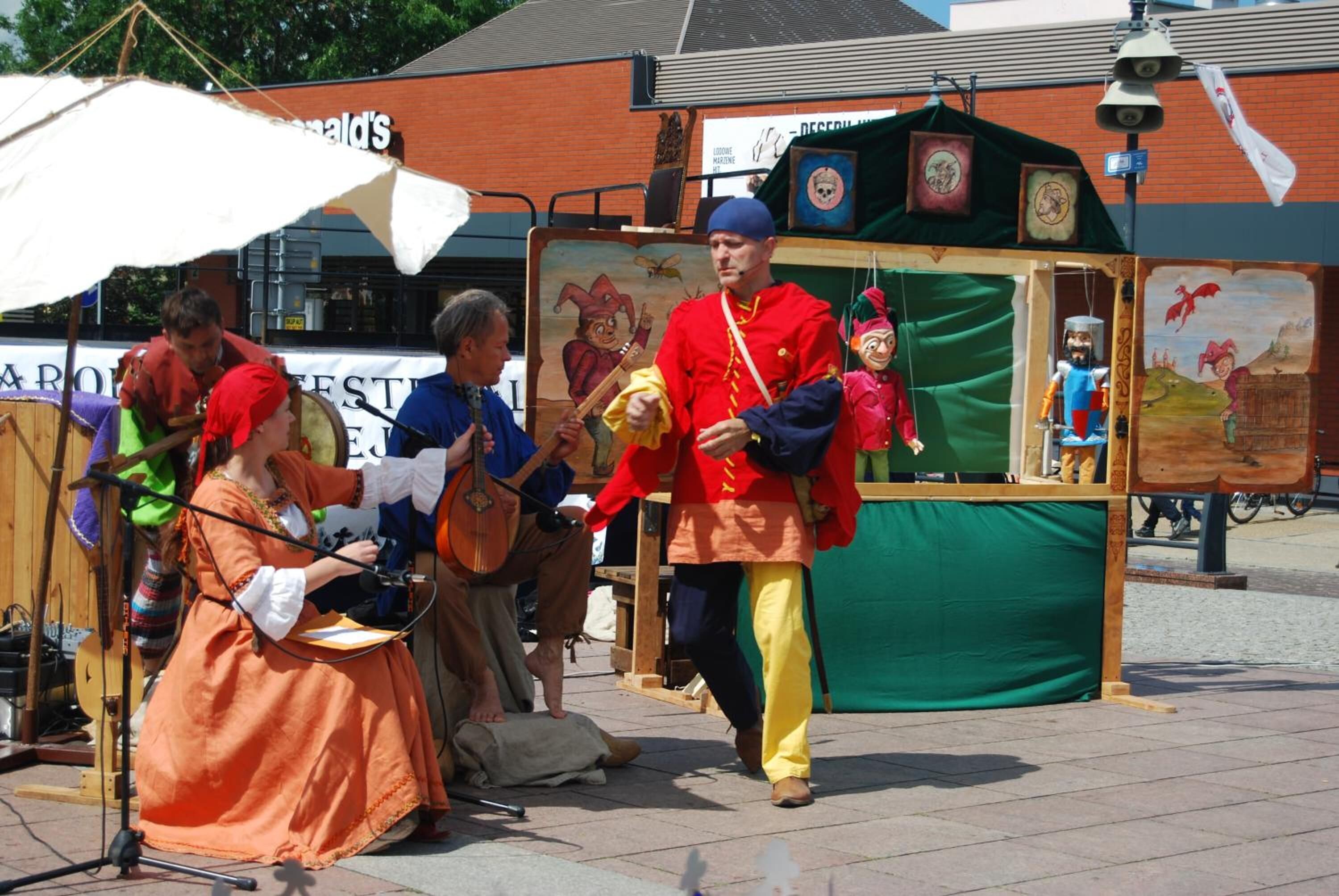 A street performance with a puppet show, a musician, and a performer in traditional attire.