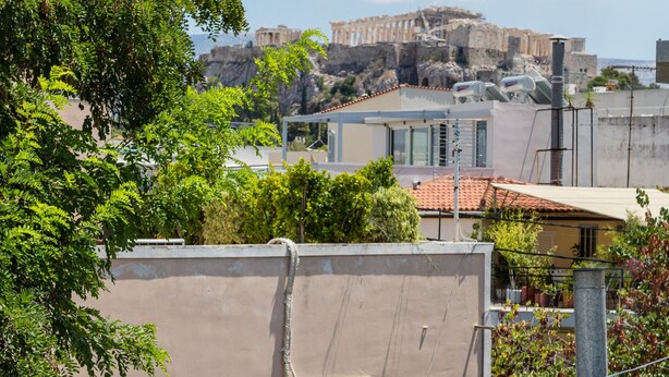 Eine Dachterrasse mit Korbmöbeln, einem runden Tisch und Blick auf eine historische Stadtansicht.