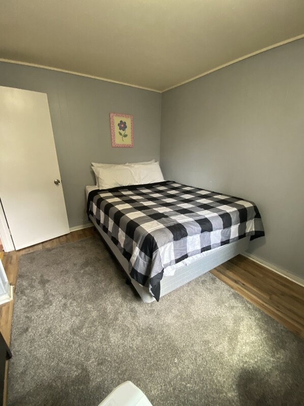 Une chambre à coucher avec un lit, une moquette grise, une porte blanche et un mur orné d’un tableau encadré.