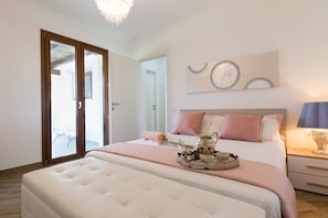 A bedroom with a large bed, a chandelier, a bedside table with a lamp, and a view through a sliding door.
