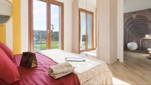 Een slaapkamer met een groot bed, uitzicht op de omgeving en een badkamer met een wastafel en spiegel.
