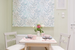 A dining area with a table set for two, a vase with flowers, and a wall with a leafy pattern. - Grandma's Chic & Bright Athenian Home with a Patio (Athens)