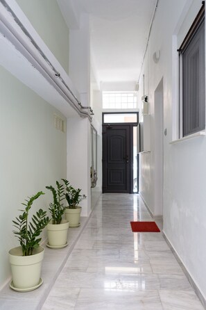 A hallway with potted plants, a red mat, and a door at the end. - Grandma's Chic & Bright Athenian Home with a Patio (Athens)