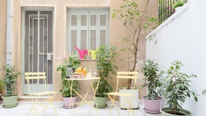 An outdoor patio with a table set for two, surrounded by potted plants and yellow chairs. - Grandma's Chic & Bright Athenian Home with a Patio (Athens)
