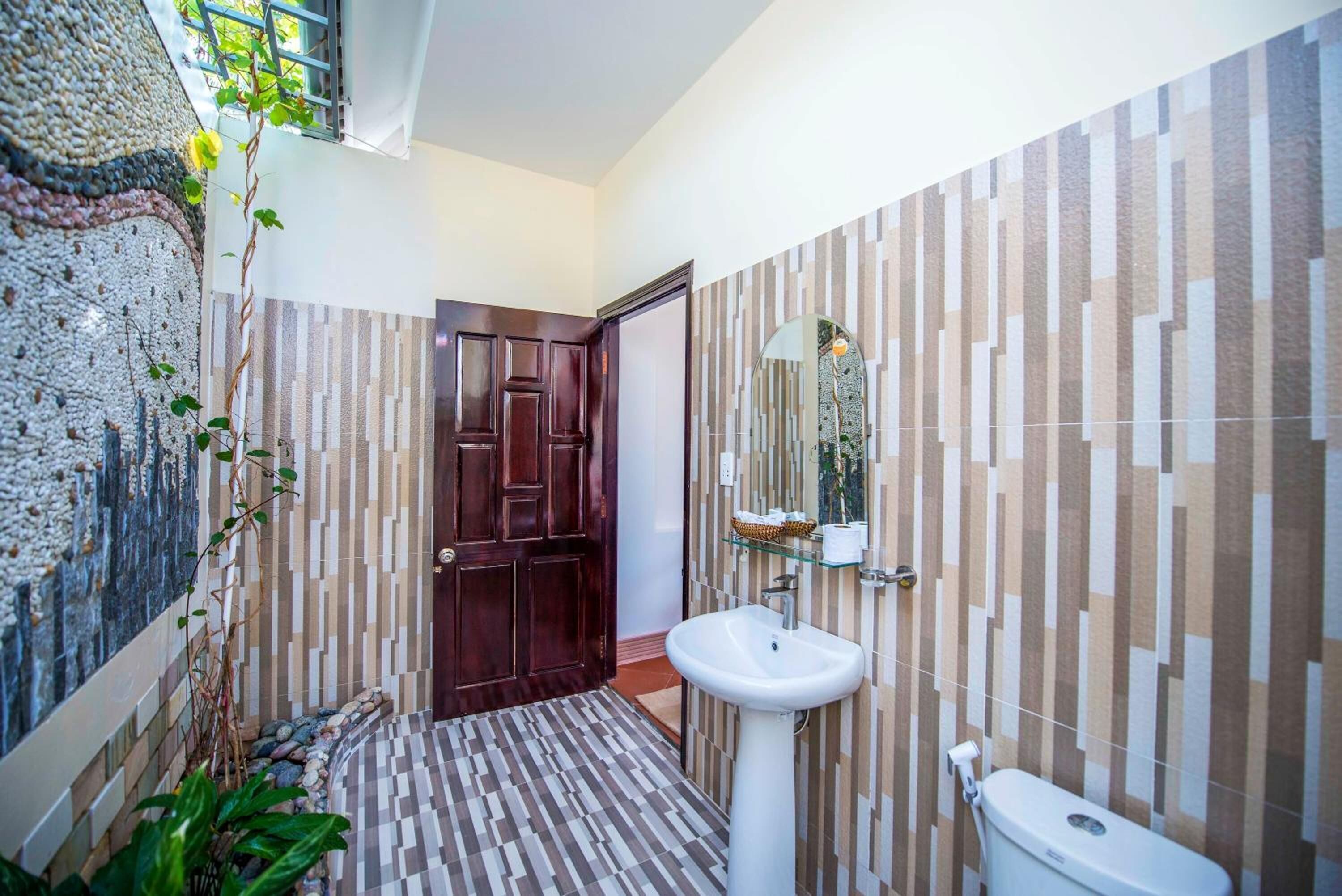 A bathroom with a wooden door, a white sink, and a tiled wall with a striped pattern.