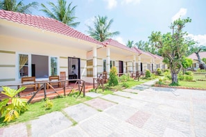 A row of hotel rooms with red-tiled roofs, wooden furniture, and a paved courtyard with palm trees.