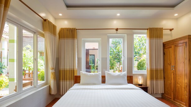 Una cama grande con ropa de cama blanca, dos mesitas de noche, un armario de madera y una ventana con cortinas.